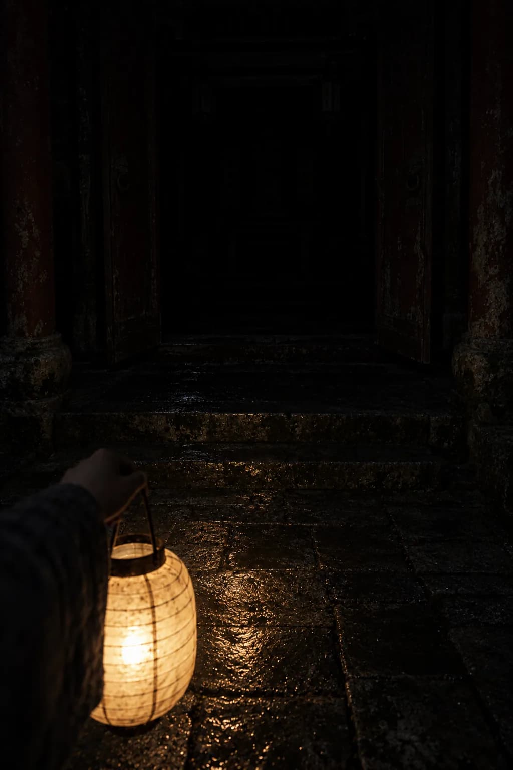 A hand carrying a lantern toward a dark doorway